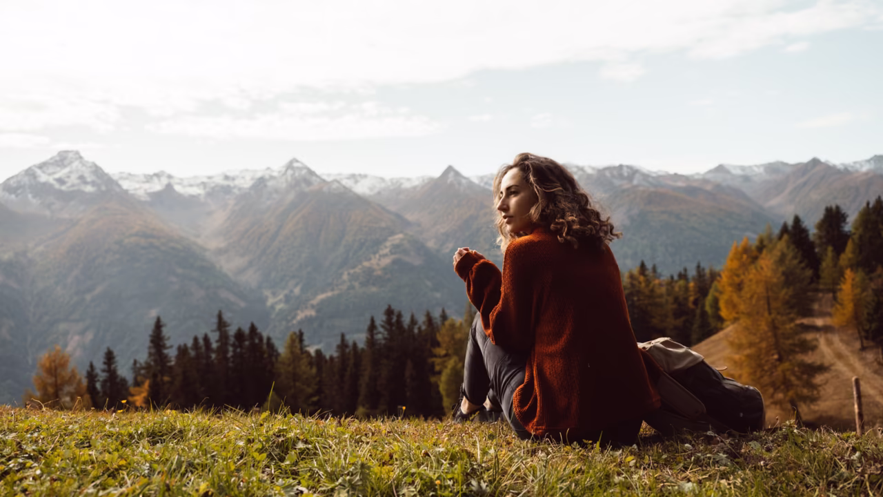 Frau sitzt auf einer Wiese in den Bergen und schaut auf das Bergpanorama